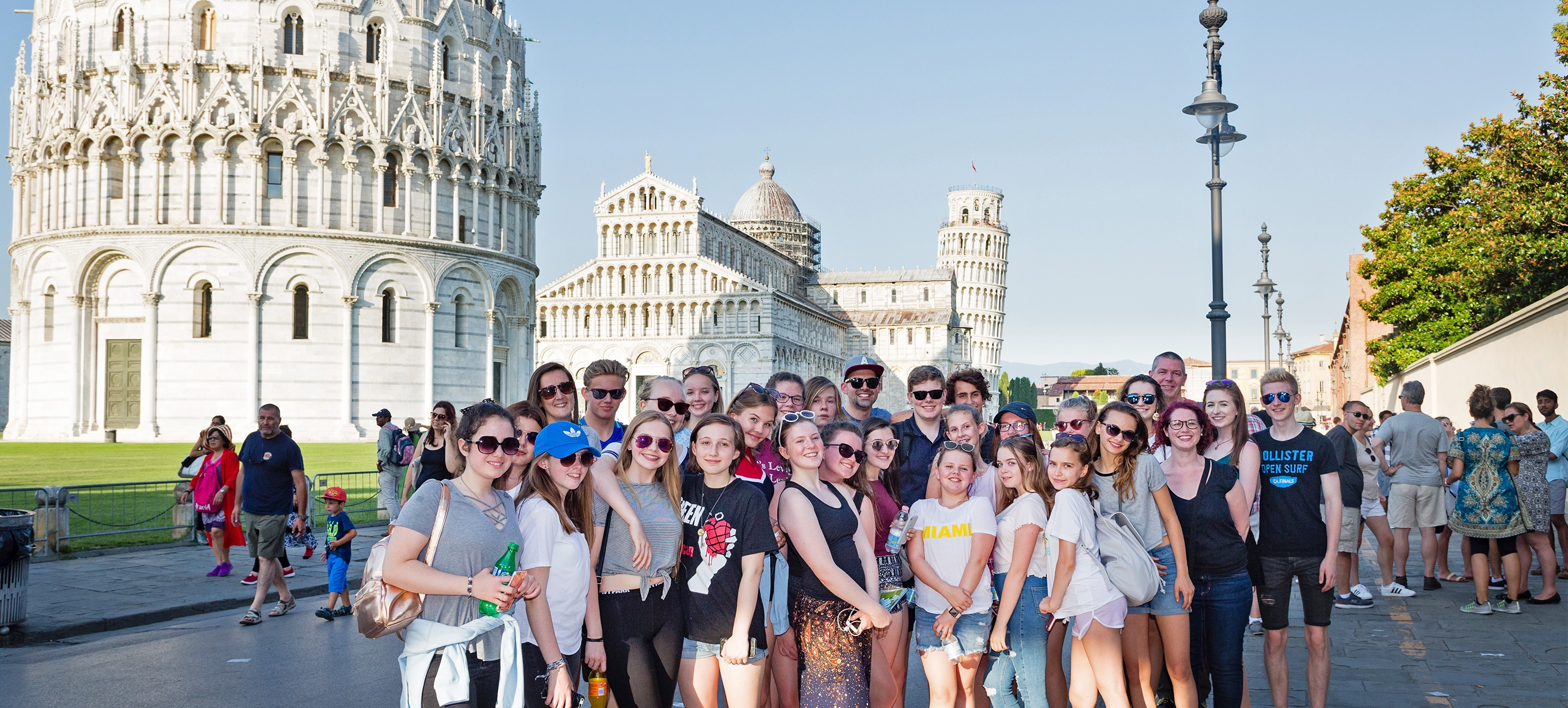 A group of young people stand in front of the leaning tower of Pisa