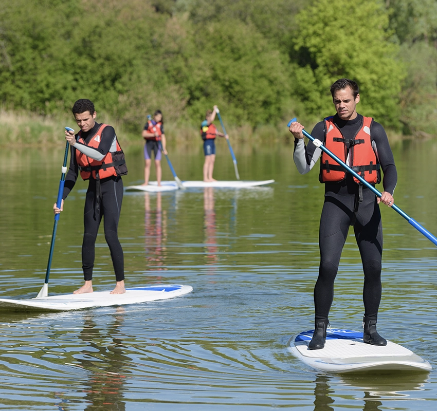 A group of people stand up paddleboarding on a like, wearing orange high vis jackets
