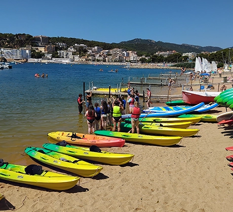Brightly coloured canoes along a beach, with students in buoyancy jackets