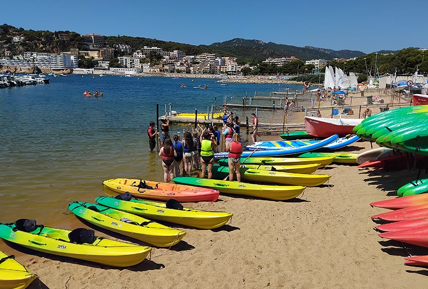 Brightly coloured canoes along a beach, with students in buoyancy jackets