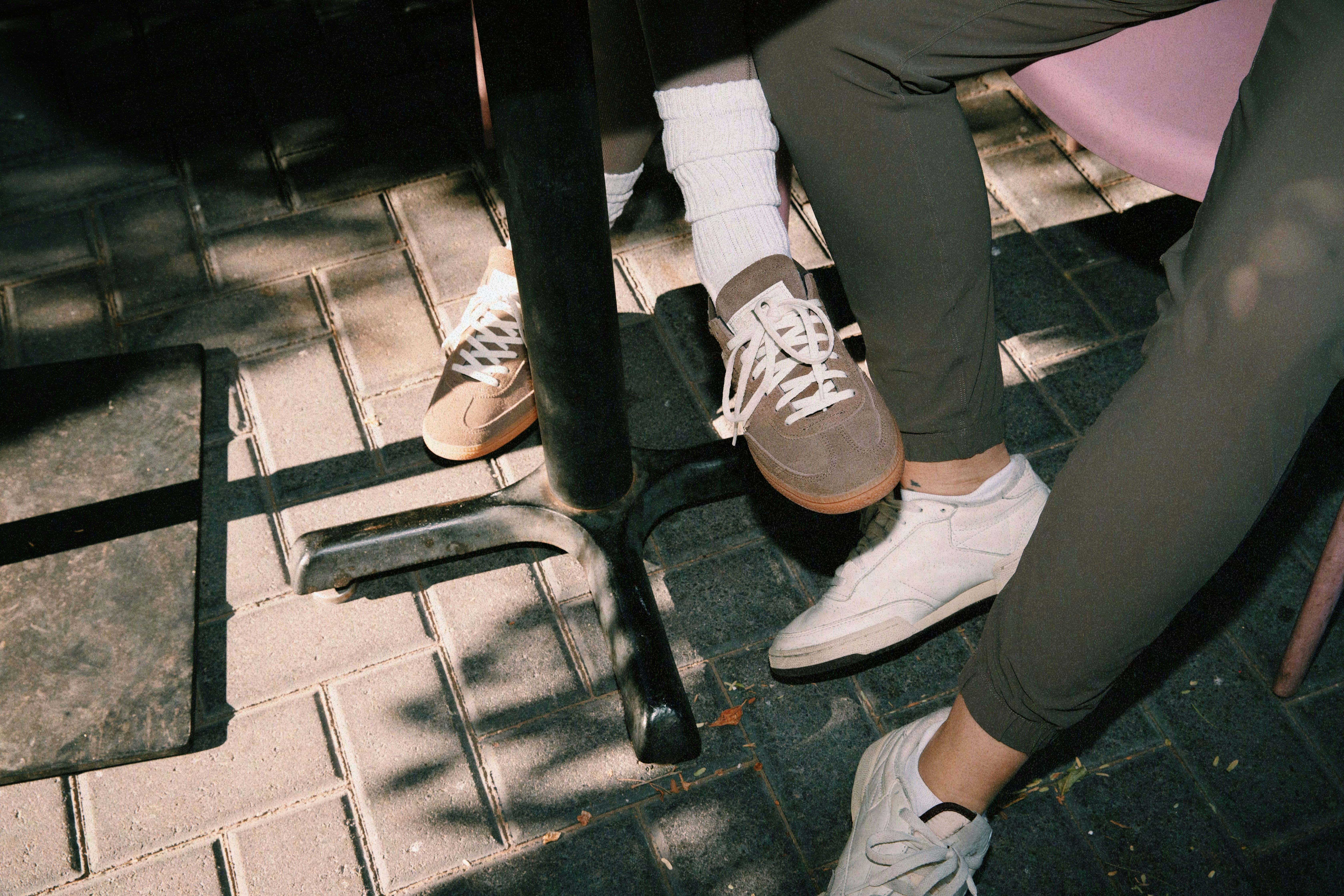 Two pairs of shoes resting on a patio floor; one is gray with white laces, and the other is white. A table leg is visible nearby.