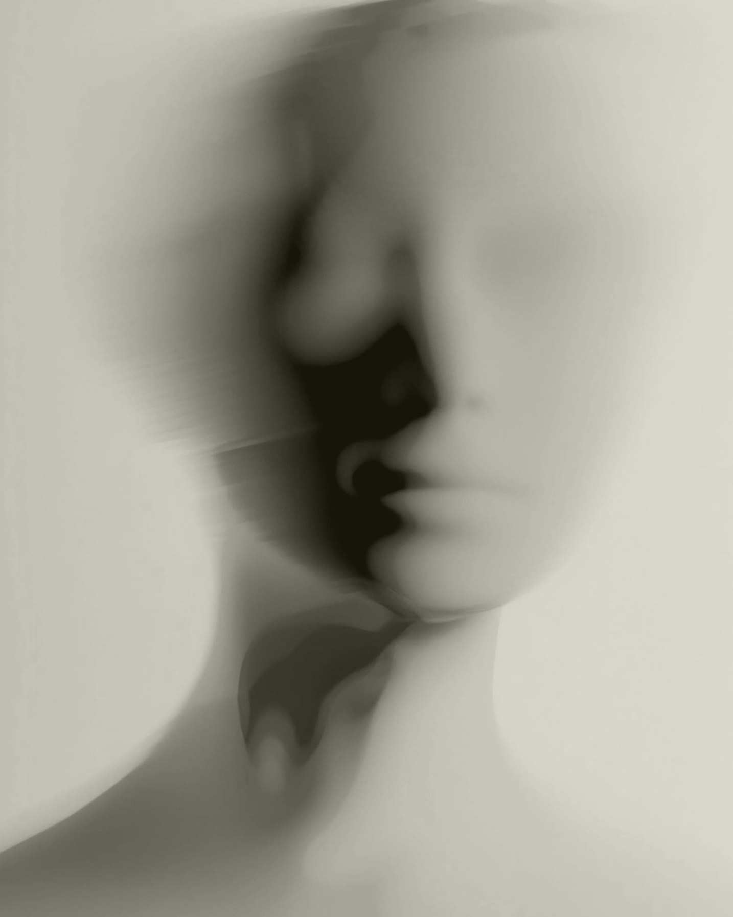 Immagine monocromatica astratta e sfocata di un volto umanoide, con tratti indistinti e ombre morbide. La figura sembra essere scultorea, fondendosi dolcemente con lo sfondo, creando un effetto etereo e onirico.