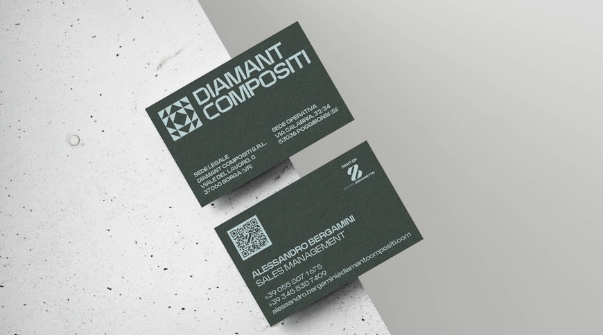 Due biglietti da visita neri su una superficie di cemento. Il biglietto in alto presenta un logo e i dettagli di Diamant Compositi, mentre quello in basso mostra il nome Alessandra Bergammi, Sales Manager, con i dettagli di contatto e un codice QR.