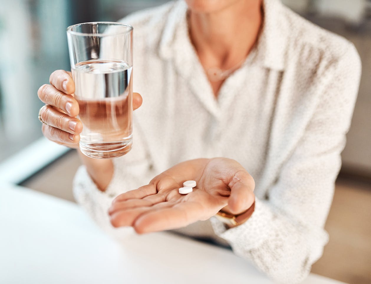 Woman with two pills in her hand and a glass of water