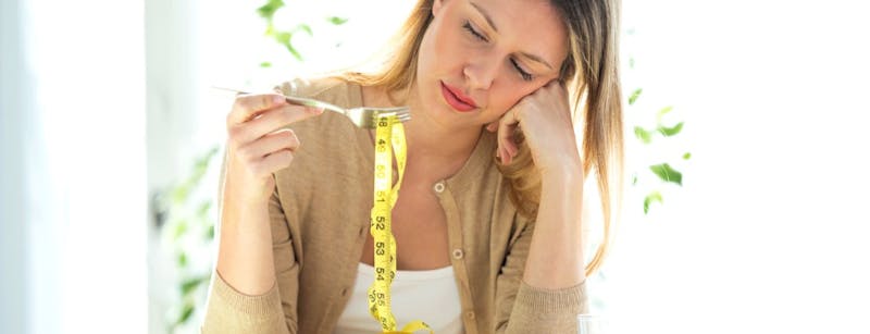 Woman looking forlorn at a bowl filed with a measuring tape.
