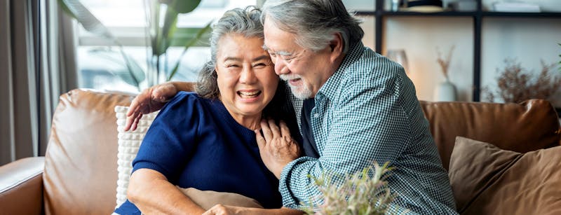 Elderly woman and man happily hugging on couch.
