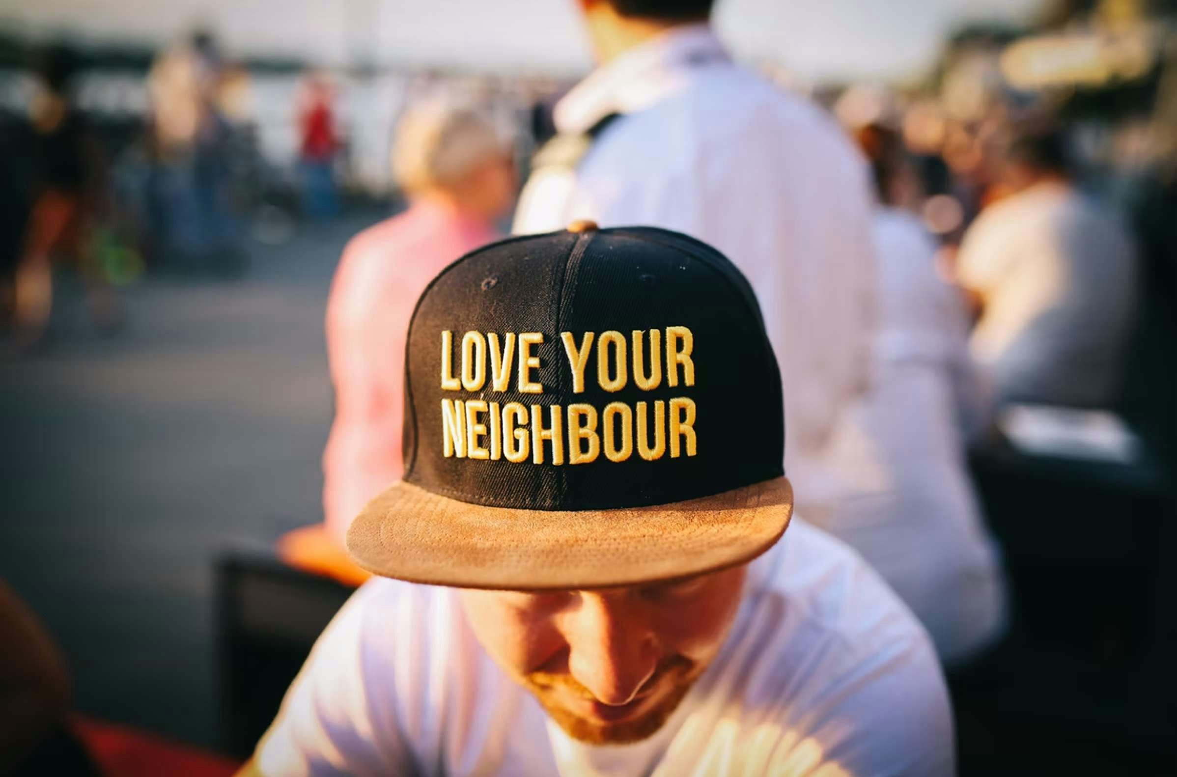 Man wearing black hat with yellow letters that say, "Love Your Neighbor"
