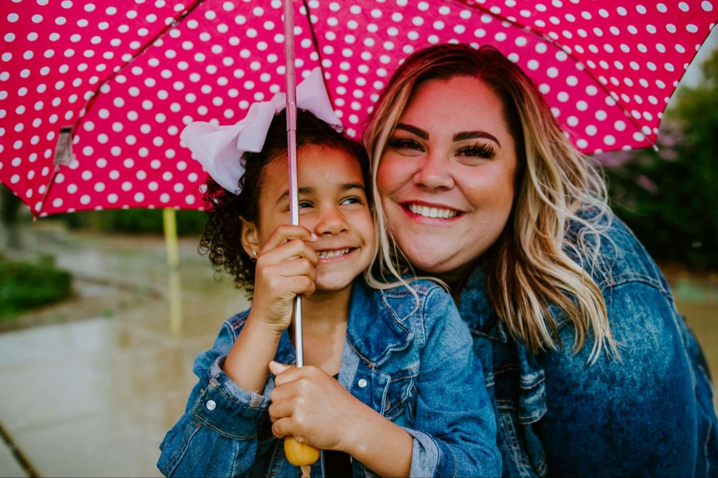 Smiling woman wearing a jean jacket beside smiling young girl holding umbrella