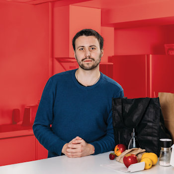 Young man standing next to bag of groceries.