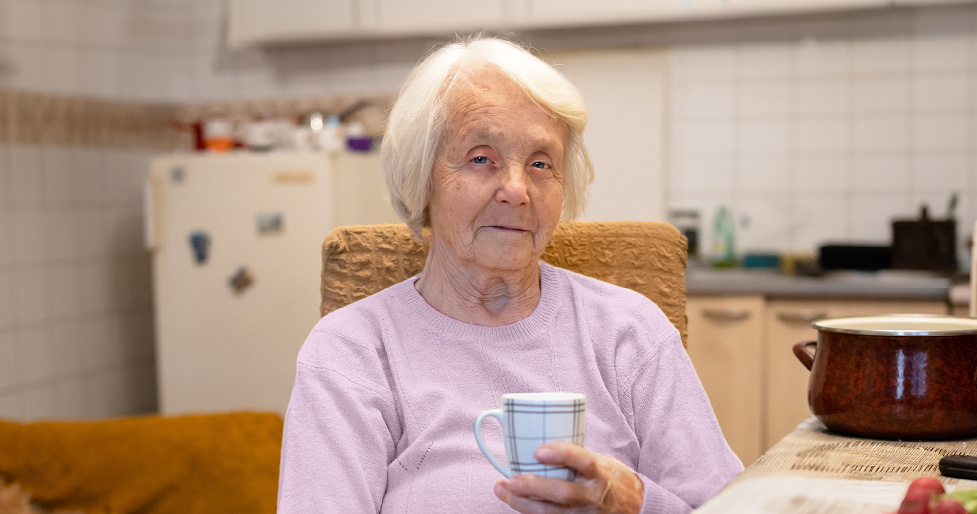 Elderly woman in pink shirt holding mug.
