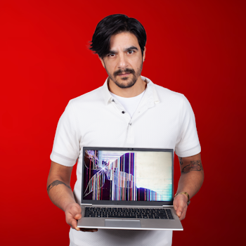 Photo of man holding laptop with broken screen on red background.