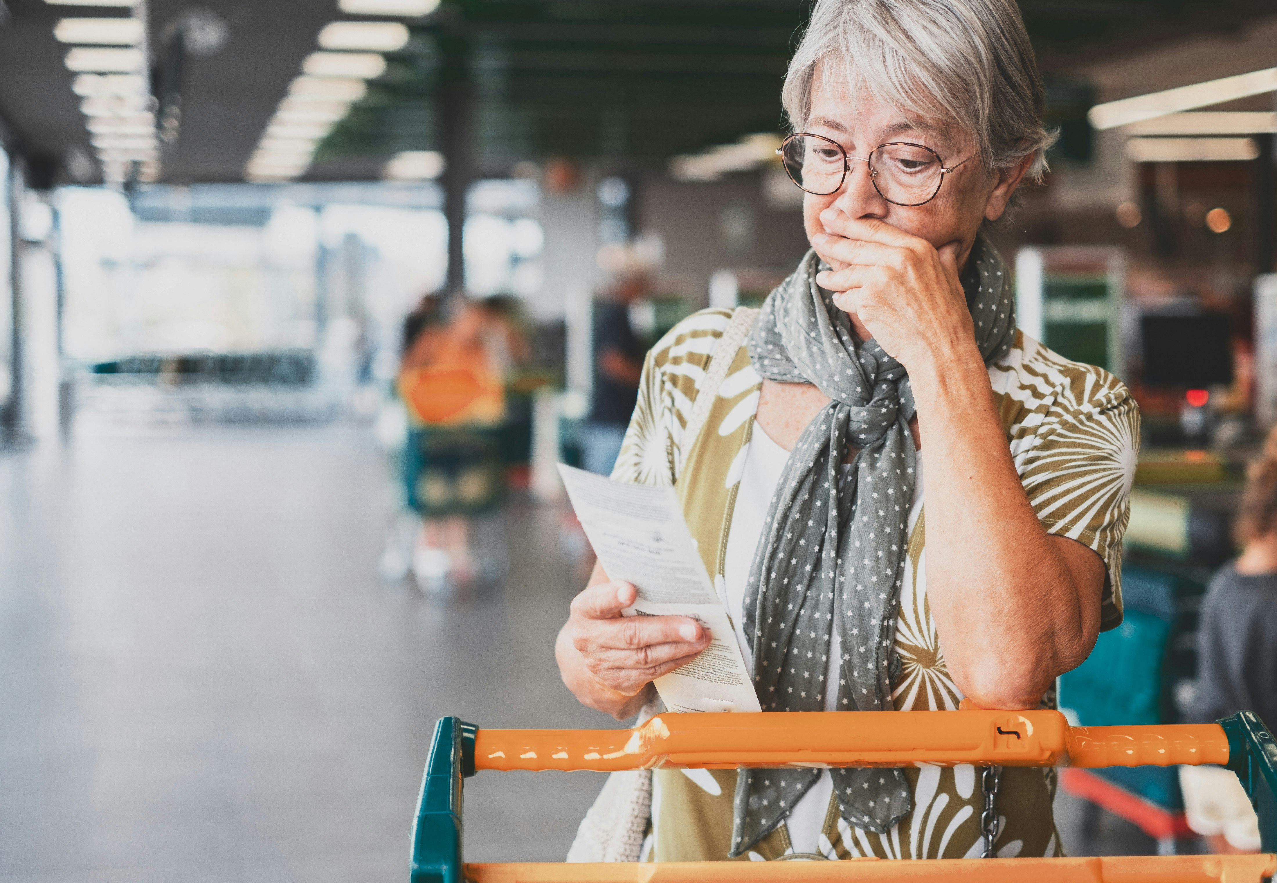 Woman with grey hair reading supermarket receipt.