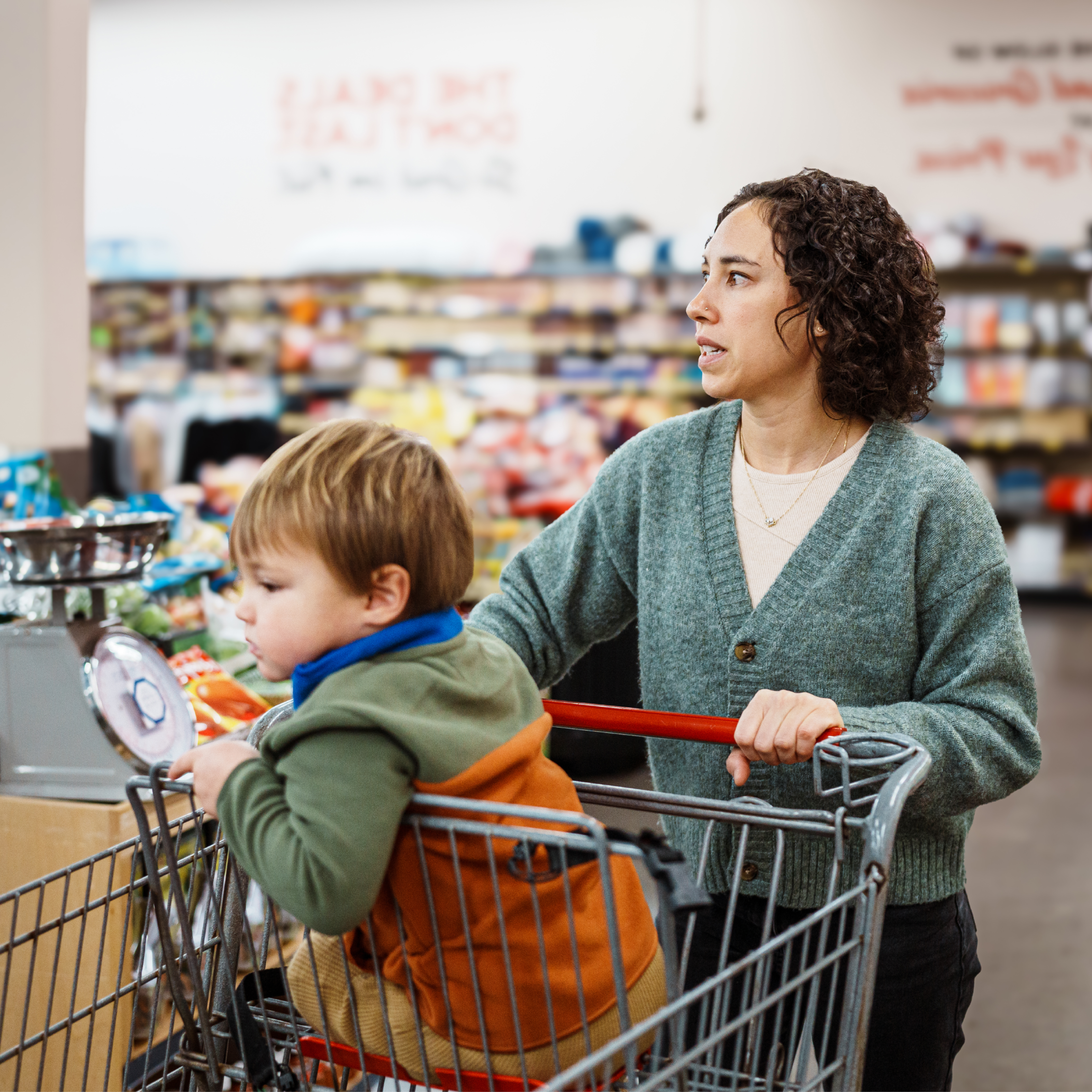 Woman with child and shopping trolley in supermarket looking worried.