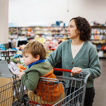 Woman with child and shopping trolley in supermarket looking worried.