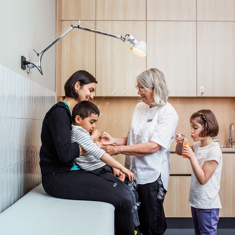 Sjuksköterska ger vacccinspruta samtidit som mamma håller honom och dotter blåser såpbubblor