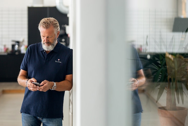 Office Man Standing Leaning Against Wall Looking At Phone