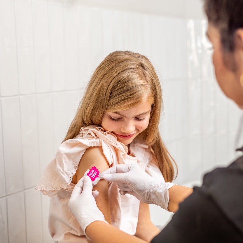 Flicka får plåster på höger överarm från sjuksköterska efter vaccination