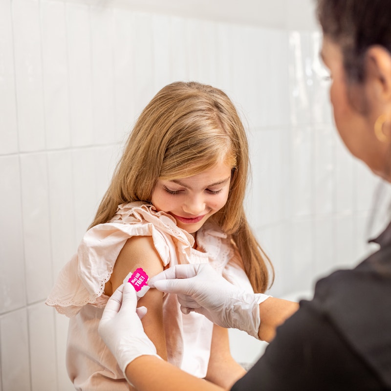 Flicka får plåster på höger överarm från sjuksköterska efter vaccination