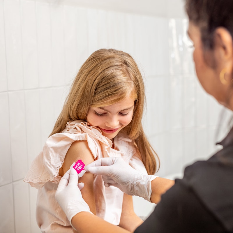 Flicka får plåster på höger överarm från sjuksköterska efter vaccination