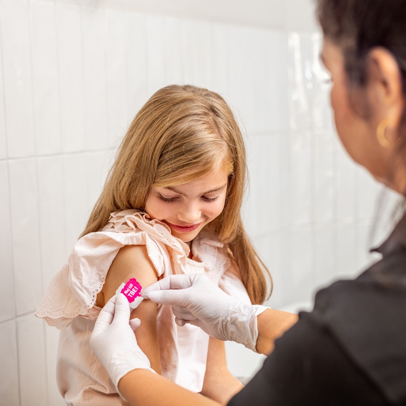 Flicka får plåster på höger överarm från sjuksköterska efter vaccination