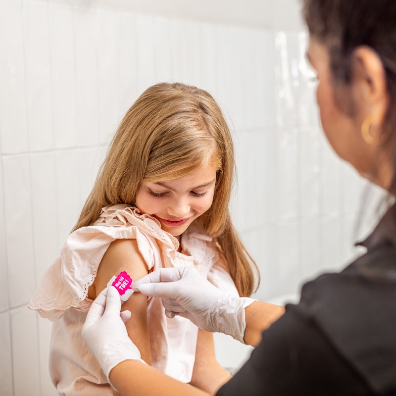 Flicka får plåster på höger överarm från sjuksköterska efter vaccination