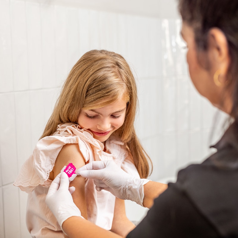 Flicka får plåster på höger överarm från sjuksköterska efter vaccination