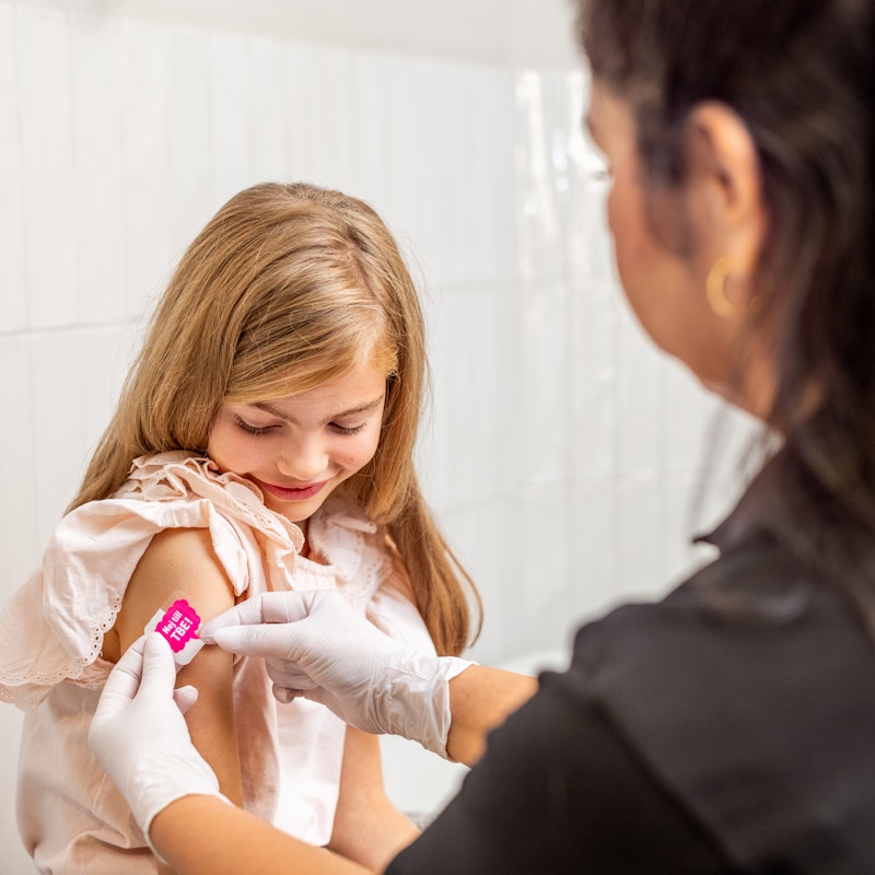 Flicka får plåster på höger överarm från sjuksköterska efter vaccination