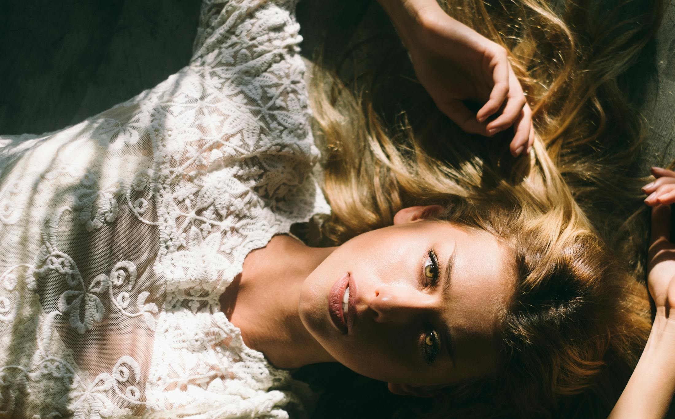 Beautiful blond model in white lying down and looking up at camera.