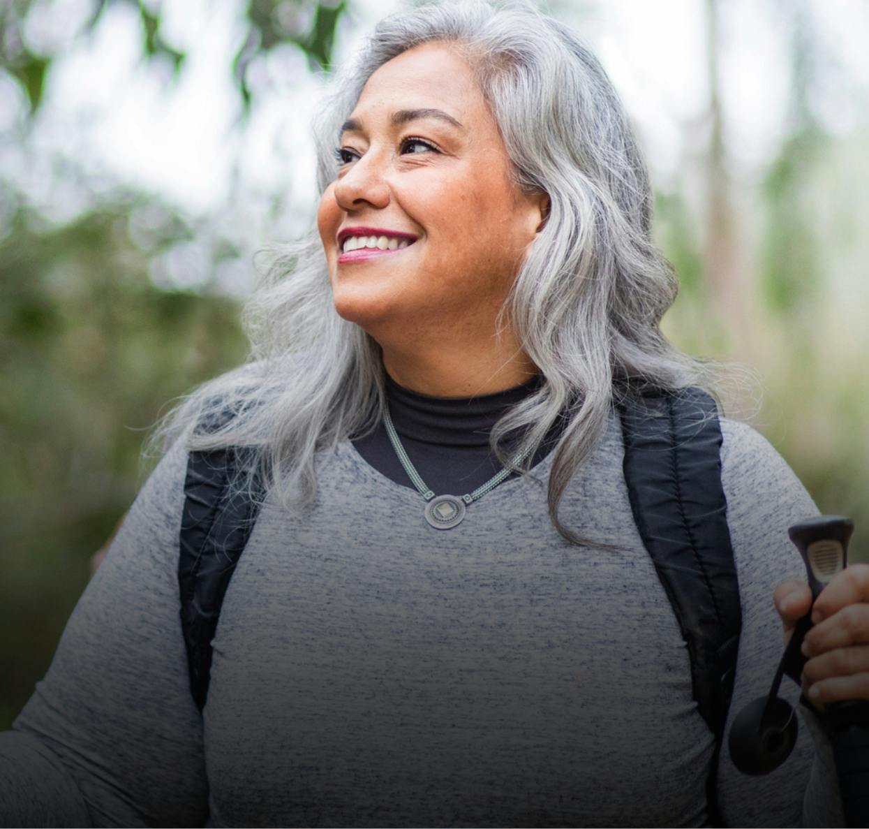 Older woman with hiking stick in hand smiling and looking off to her right.