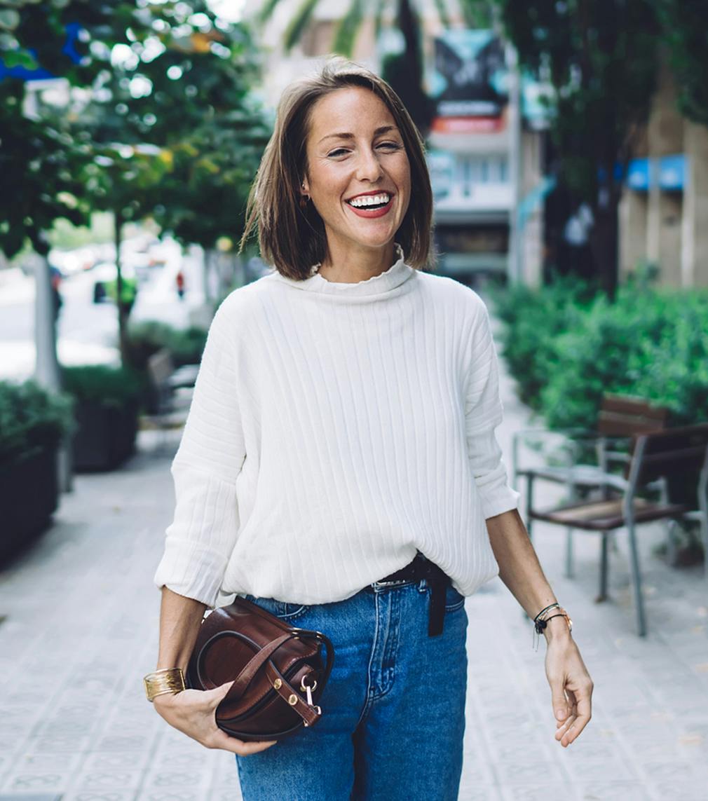 Woman in jeans and a white shirt smiling while standing on the sidwalk