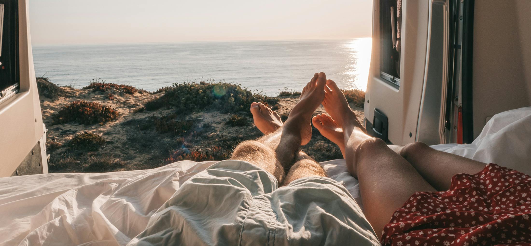 A couple with their legs hanging out of their van overlooking the ocean