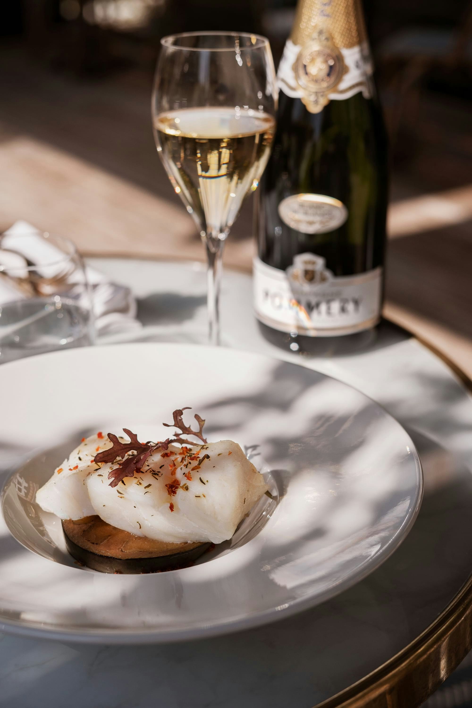 Bottle of Pommery Apanage Blanc de Blancs with glass and plate on table