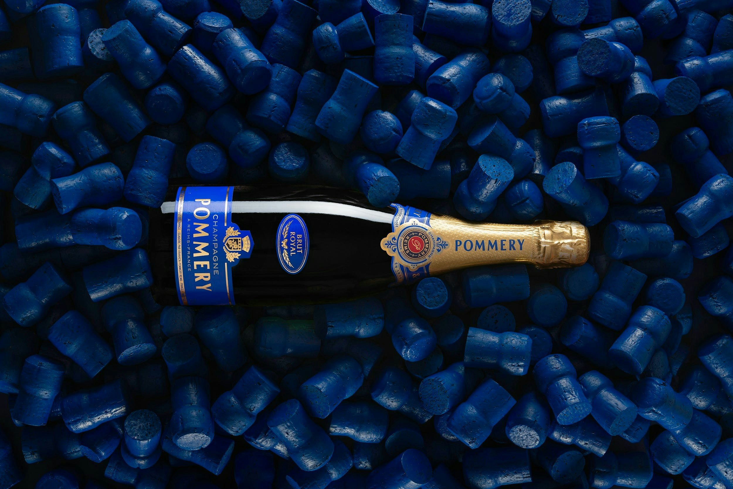 Une bouteille de Pommery Brut Royal 75cl sur fond bleu composé de bouchons bleus
