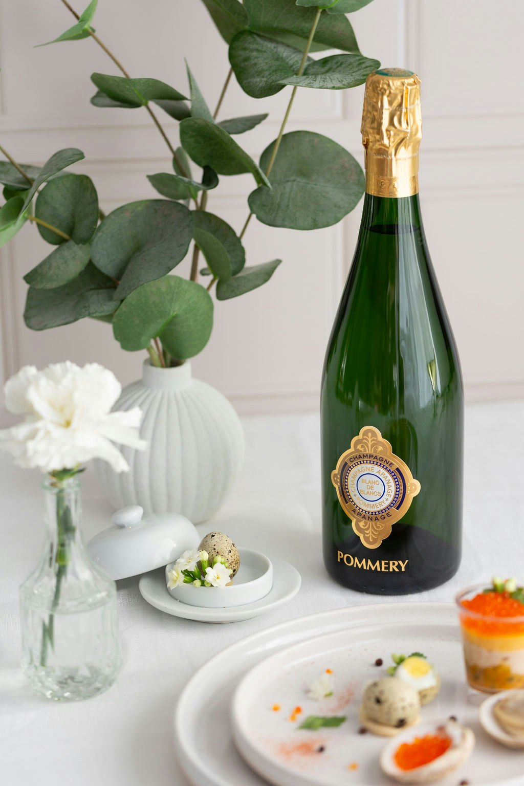 Une bouteille de Pommery Apanage Blanc de Blancs 1874 sur une table avec une assiete et des plantes