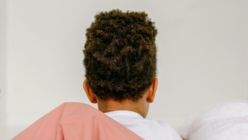 Ein kleines Kind mit lockigem Haar, von hinten gesehen, faulenzt bequem drinnen.