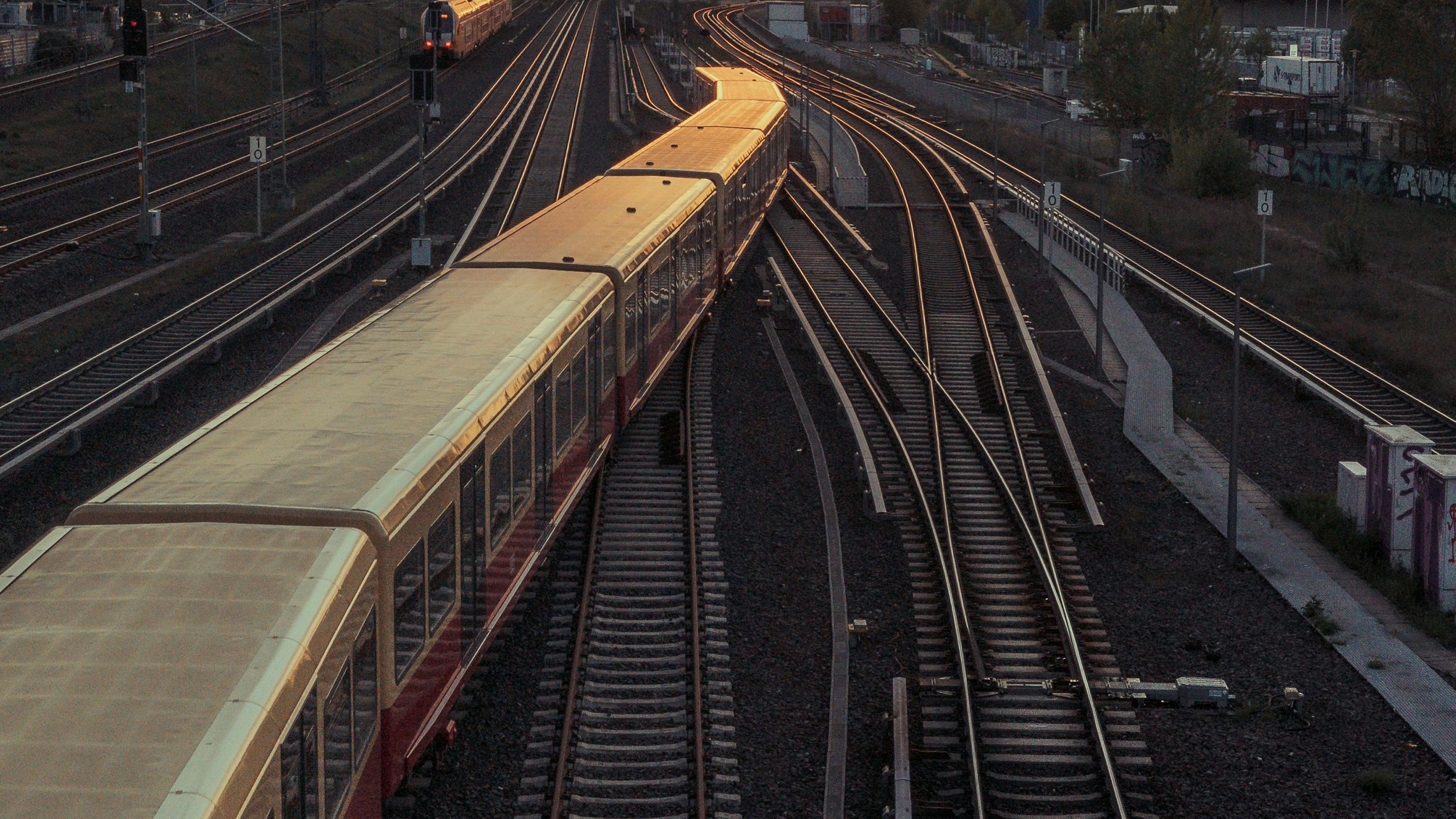 Ein Zug auf Bahngleisen bei Sonnenuntergang mit städtischer Skyline und Fernsehturm.