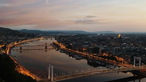 Fesselnde Luftaufnahme von Budapest in der Abenddämmerung mit beleuchteten Brücken und der ruhigen Donau.