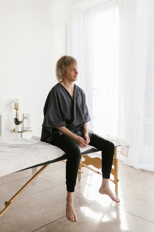 Erwachsener sitzt auf einem Massagetisch in einer ruhigen Spa-Umgebung mit natürlichem Licht.