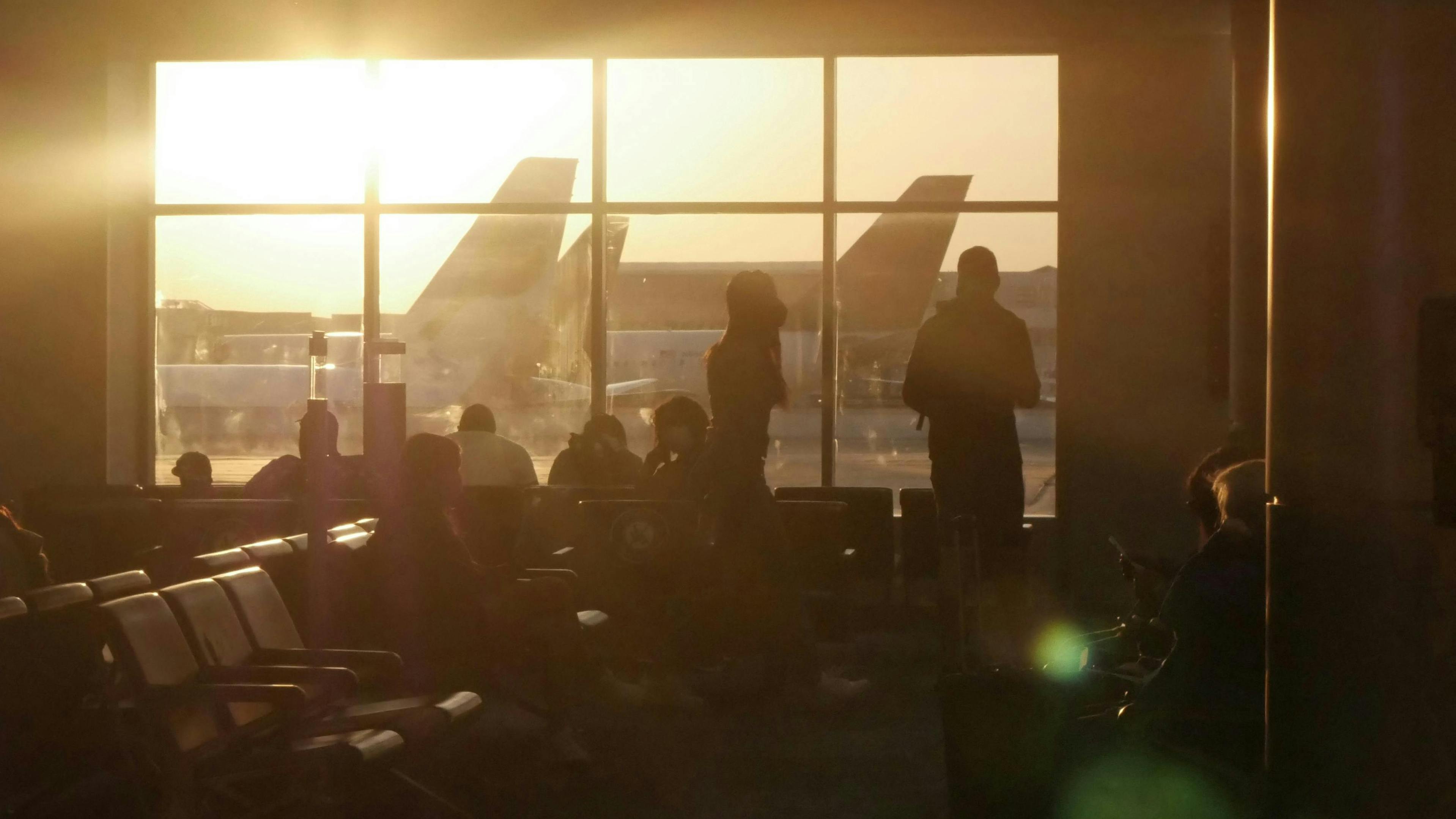 Passagiere warten am Flughafen Orlando auf ihre Flüge, im Hintergrund ist der Sonnenuntergang zu sehen, der Silhouetten erzeugt.
