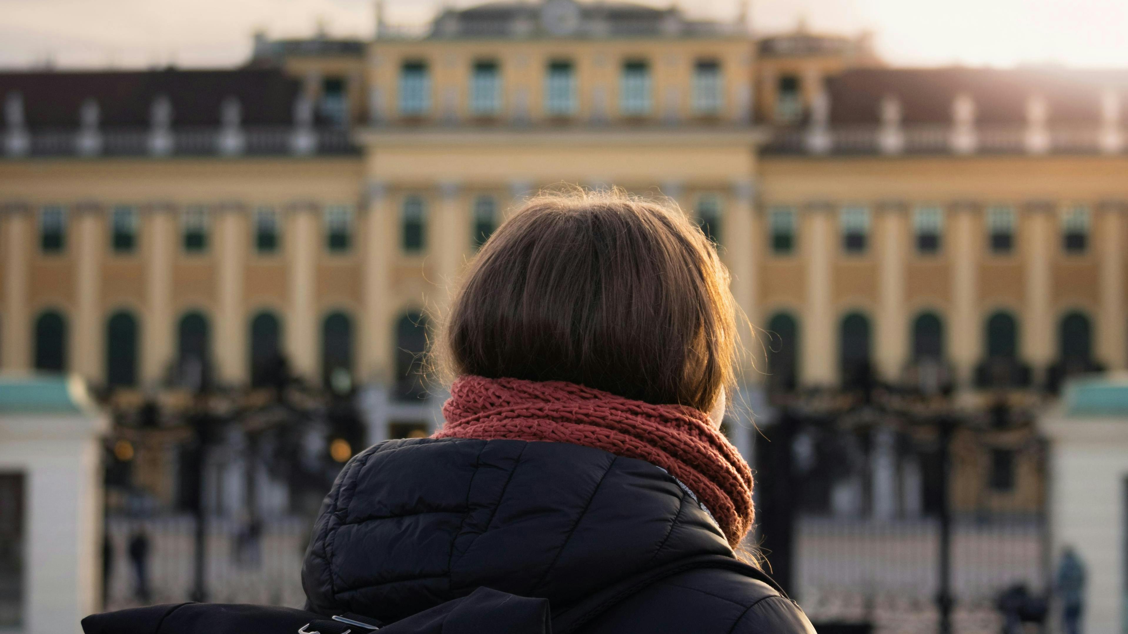 Eine Frau steht bei Sonnenuntergang vor dem historischen Schloss Schönbrunn in Wien und fängt die architektonische Pracht ein.