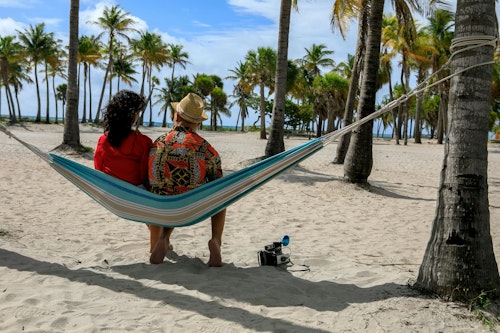 Ein Paar genießt einen ruhigen Moment auf einer tropischen Strandhängematte unter Palmen.