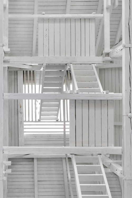 Innenaufnahme einer weißen Holzkonstruktion mit mehreren Treppen und Balken.