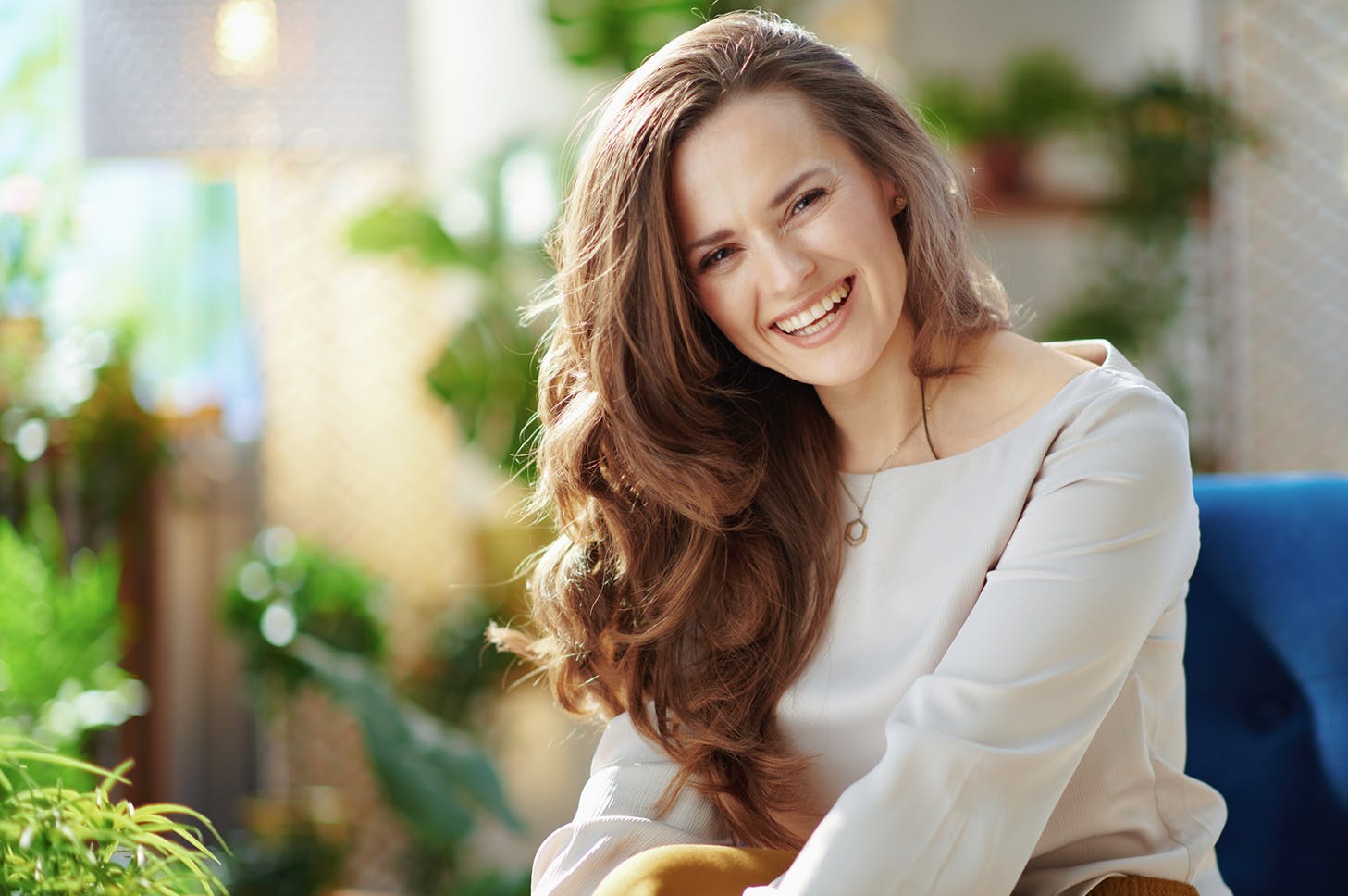 smiling woman sitting on a blue chair with a plant in the background