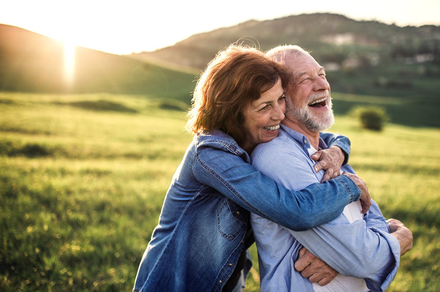 older couple are hugging each other in a field of grass
