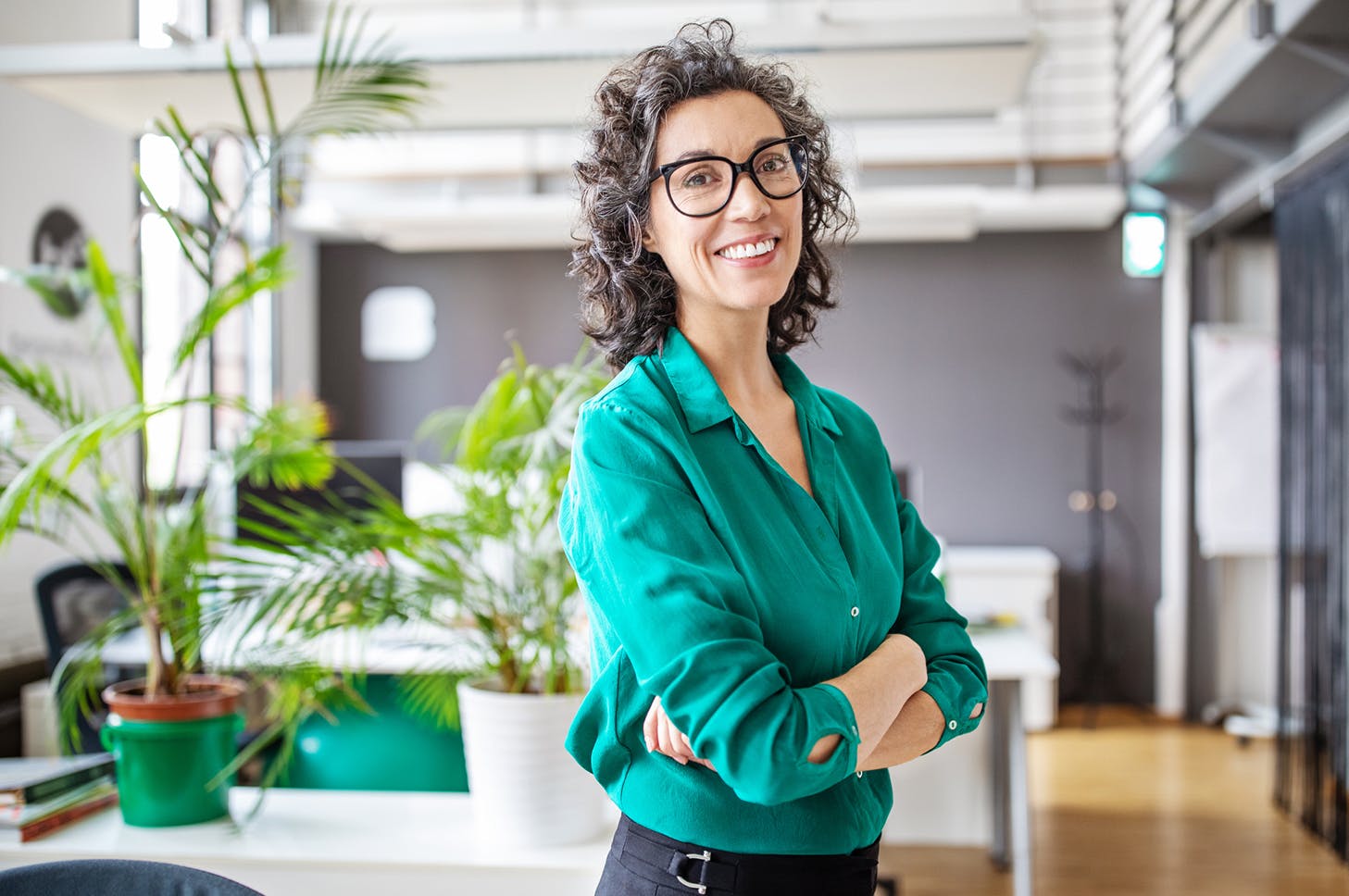 smiling woman in green shirt and black pants standing in an office