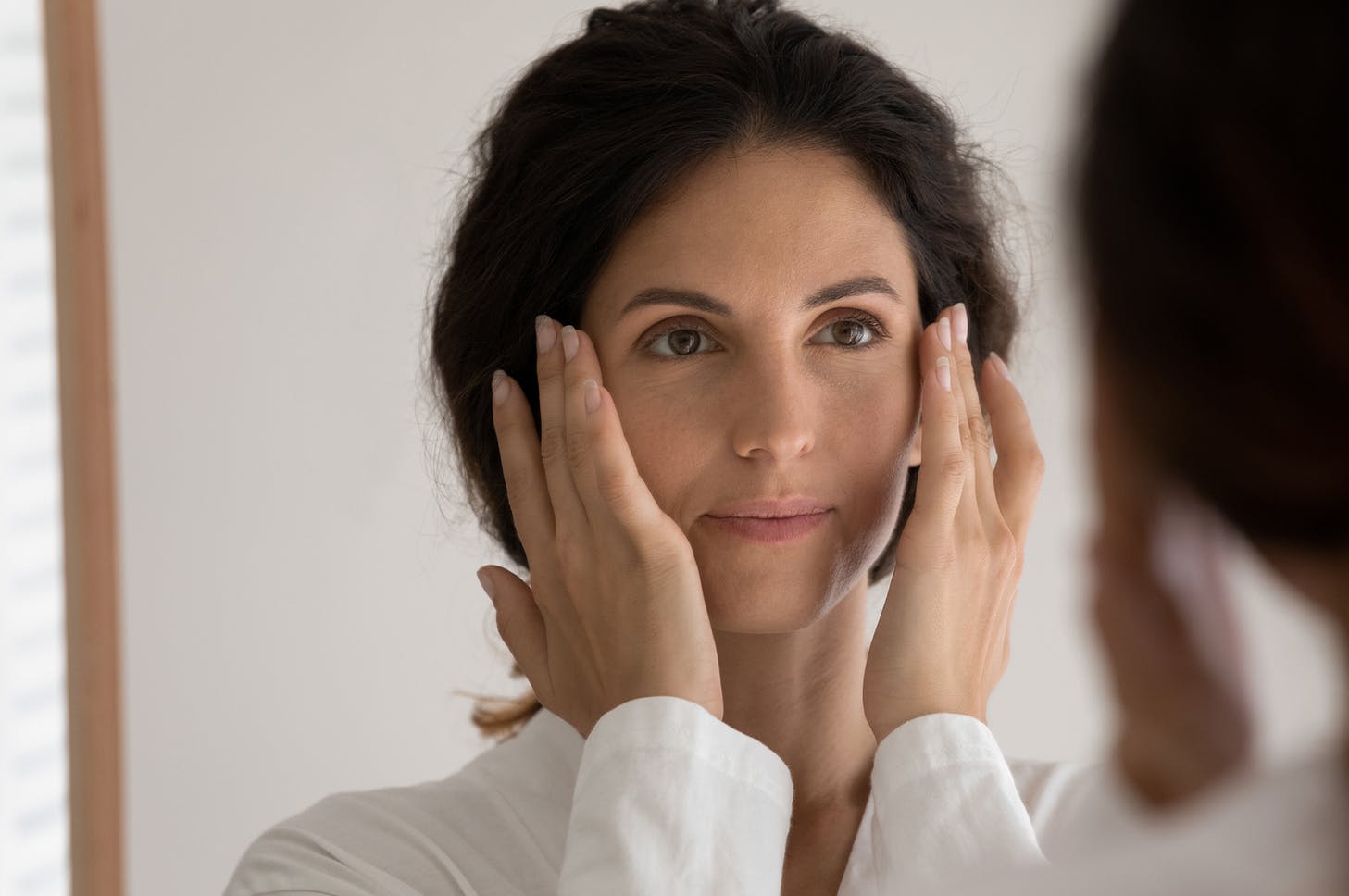 a close up of a woman looking at her eyes in the mirror with her hands on her temples