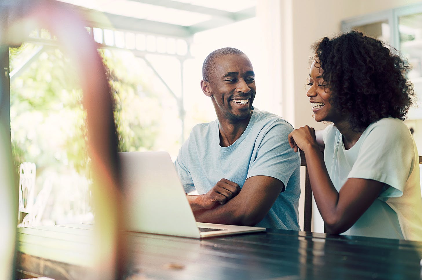 wife and husband smiling while looking at each other and in front of a laptop