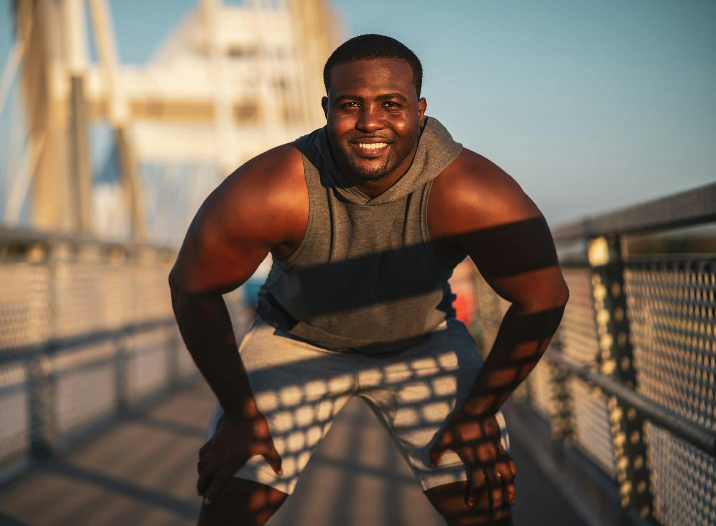 Man smiling with his hands on his knees while on a bridge