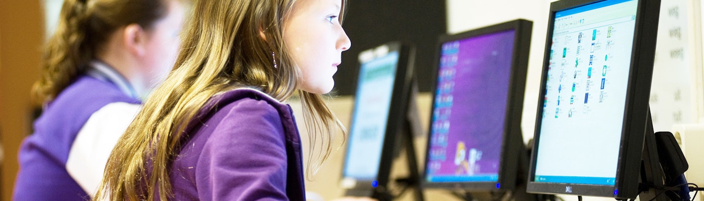 Op de afbeelding staat een meisje die achter een computer zit en geconcenteerd aan het werk is