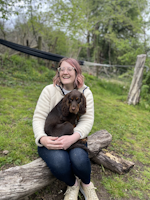 Fiona McLaren is sat on a piece of wood smiling with her dog Spud in her arms
